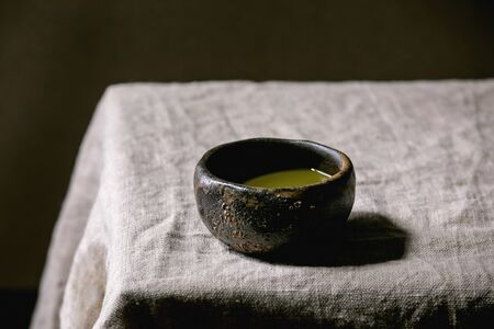 Japanese matcha green tea in wabi sabi ceramic cup with pink magnolia flowers on grey linen table cloth.の写真素材
