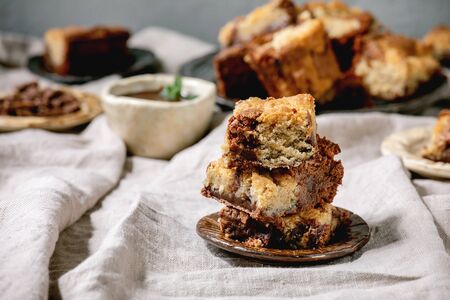 Trend baking Brookies chocolate brownies and cookies homemade cake sliced by squares in different ceramic plates, chocolate sauce, wooden spoons on grey linen table clothの写真素材