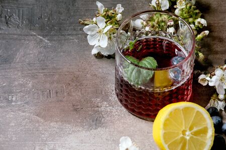 Cocktail glass with blueberry sparkling cider or lemonade with sliced lemon, blueberries and mint. Blossom branches above. Gray texture background.の写真素材