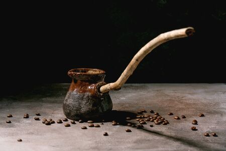 Black turkish coffee in craft handmade ceramic coffee pot cezve with long wooden handle with coffee...