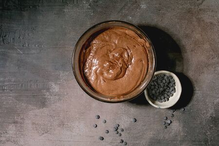 Dough for home baking classic dessert brownies in glass bowl, with chocolate chips over grey texture background. Flat lay, spaceの写真素材