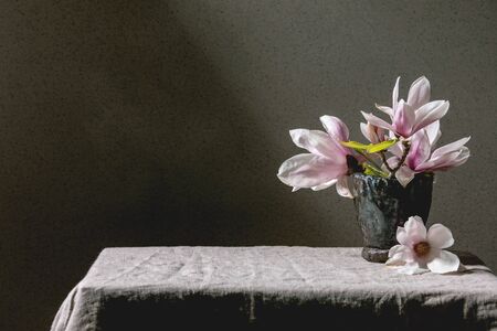 Bouquet of beautiful pink magnolia flowers on branches with new leaves in ceramic vase, standing on gray linen table cloth. Copy spaceの写真素材