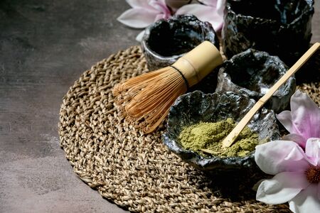 Japanese matcha green tea powder in craft ceramic bowl, couple of cups, bamboo whisk and pink...