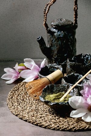 Japanese matcha green tea powder in craft ceramic bowl, couple of cups, bamboo whisk, ceramic teapot...