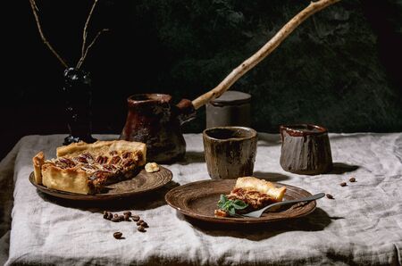 Piece of home baking classic american pecan caramel pie on ceramic plate, coffee cup, cezve, jug of cream on gray linen table cloth..の写真素材