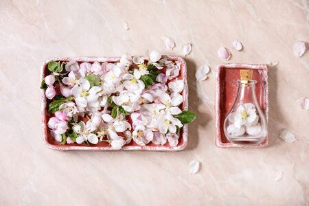 Flat lay of spring apple blooming flowers and petals in ceramic tray, glass bottle with flowers over pink marble background. Perfume floral scent concept. Copy spaceの写真素材