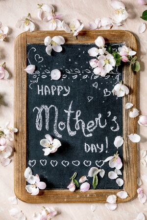 Mother's day greeting card. Vintage chalkboard with handwriting lettering Happy mother's day with spring apple flowers and petals over pink marble background. Flat lay, spaceの写真素材