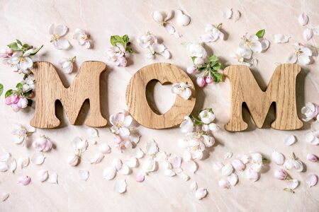 Mother's day greeting card. Wooden letters MOM with spring apple flowers and petals over pink marble background. Flat lay, spaceの写真素材