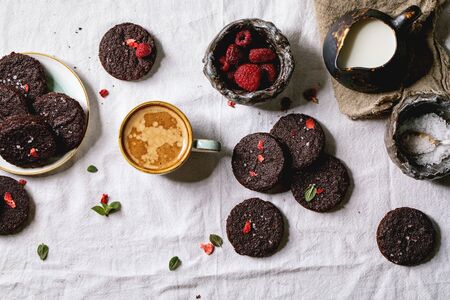 Homemade dark chocolate salted brownies cookies decorated by dried and fresh raspberries, with salt flakes, berries, mint, milk and cup of coffee over white cotton cloth. Flat lay, spaceの写真素材