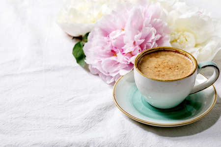 Cup of espresso coffee, pink and white peonies flowers with leaves over white cotton textile background.の写真素材