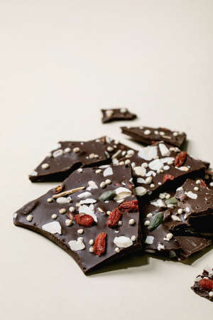 Handmade chopped dark chocolate with different superfood additives seeds and goji berries over beige...