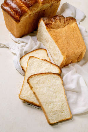 Homemade Hokkaido wheat toast bread whole and sliced on white cloth on table.