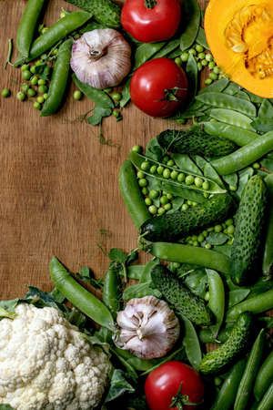 Variety of fresh raw organic vegetables for cooking. Half of hokkaido pumpkin, young green pea, cauliflower, garlic, cucumbers , tomatoes over wooden background. Farmer market concept. Flat lay, spaceの写真素材