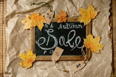 Autumn sale concept. Vintage chalkboard with hand written lettering Sale, labels with percents, yellow autumn leaves over craft crumpled paper. Flat lay.の写真素材