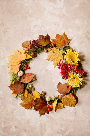 Beautiful Autumn botanical wreath composition creative layout with flowers, moss and yellow autumn leaves over beige concrete background. Flat lay, copy spaceの写真素材