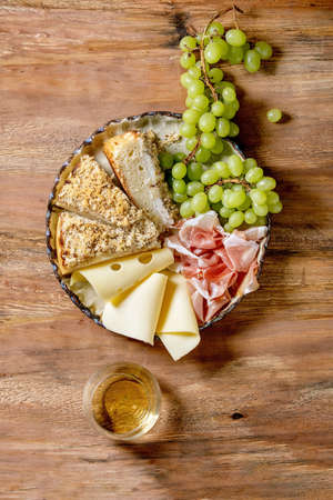 Appetizers antipasti with white sicilian focaccia. Traditional bread sliced cake with onion served with prosciutto ham, cheese, grapes and glass of white wine over wooden background. Flat lay, spaceの写真素材