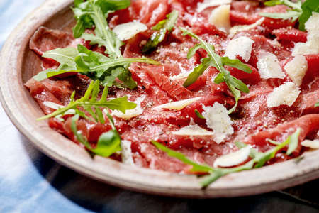 Classic beef carpaccio with cheese and arugula on ceramic plate over white and blue tablecloth.の写真素材