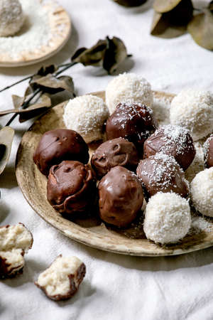 Raw vegan homemade coconut chocolate candy balls with coconut flakes in ceramic plate over white...