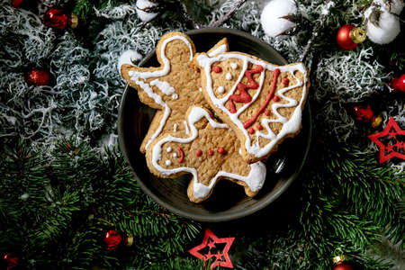 Homemade traditional Christmas gingerbread cookies with icing ornate. Gingerbread Man, angel, bell on ceramic plate with xmas decorations and fir tree as background. Flat layの写真素材