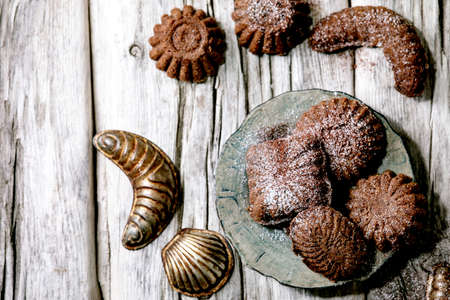 Homemade traditional shortcrust cookies chocolate crescents with cocoa icing sugar in ceramic plate with cookie molds over old wooden background. Flat lay, spaceの写真素材