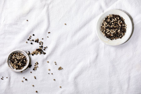 Mix of black and white peppercorns seasoning pepper spices in white plate on wooden board. White cloth as background. Flat lay, spaceの写真素材
