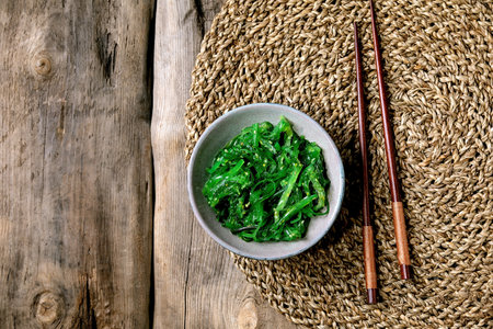 Japanese Wakame chuka seaweed salad with sesame seeds in ceramic plate with chopsticks over old wooden background. Flat lay, copy spaceの写真素材