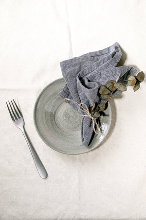 Empty ceramic plate with fork and textile napkin, decorated by eucalyptus branch over white linen tablecloth. Table setting. Flat lay, space.の写真素材