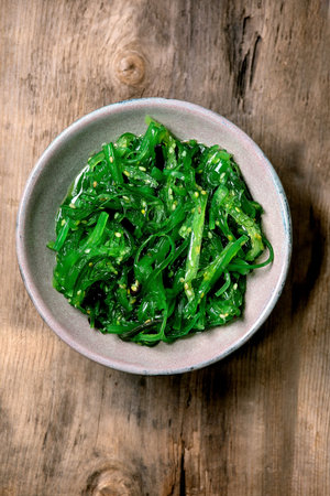 Japanese Wakame chuka seaweed salad with sesame seeds in ceramic plate over old wooden background. Flat lay, copy spaceの写真素材