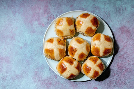 Homemade Easter traditional hot cross buns on ceramic plate over blue texture background. Flat lay,...