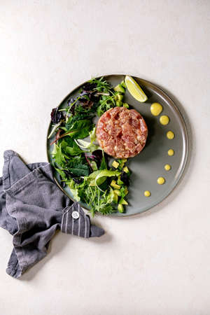 Tuna tartare with green salad, lime, avocado and mustard sauce serving on ceramic plate over white texture background. Flat lay, copy space. Fine dining, restaurant appetizerの写真素材