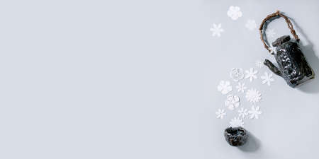 Banner creative layout with variety of white paper flowers flowing from ceramic teapot to cup over gray background. Flat lay, copy space. Flower tea, summer or spring time conceptの写真素材