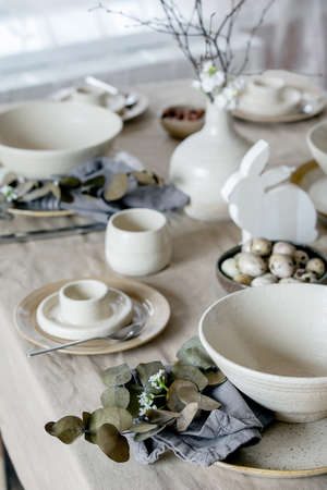 Rustic Easter table setting with empty craft ceramic tableware, plates and bowls, Easter bunny rabbit decorations, branches in vase on linen tablecloth in front of the window. Easter holiday dinner.の写真素材
