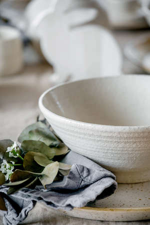 Rustic Easter table setting with empty craft ceramic tableware, plates and bowls, Easter bunny rabbit decorations, branches in vase on linen tablecloth in front of the window. Easter holiday dinner.の写真素材