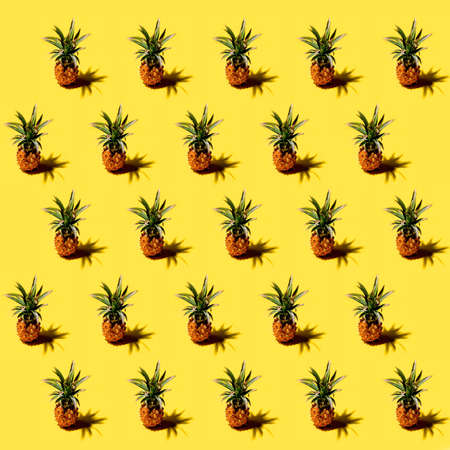 Fresh mini pineapples ananases with shadows on a bright solid yellow background pattern. Tropical style, summer conceptの写真素材
