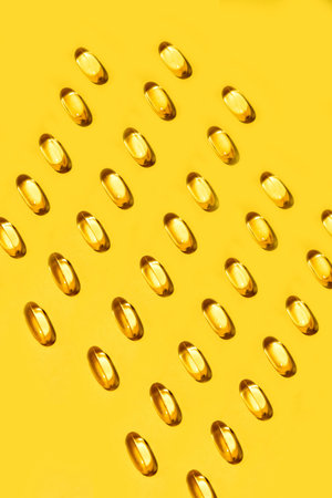 Yellow oval pills capsules vitamin Omega 3 over bright solid yellow background patternの写真素材