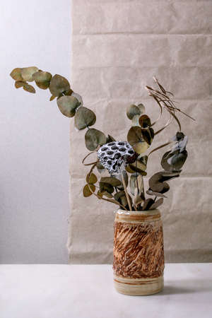 Dry flowers, eucalyptus and twigs branch in brown ceramic vase on white marble table with gray wall behind. Copy space.の写真素材