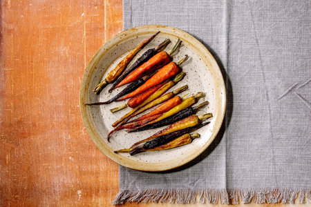 Grilled different colored carrots on ceramic plate with grey textile napkin over orange stone background. Top view, flat lay. Copy space. Vegan dinnerの写真素材