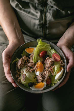 Woman hold in hand bowl of nicoise salad with canned tuna fish, olives and eggs.の写真素材