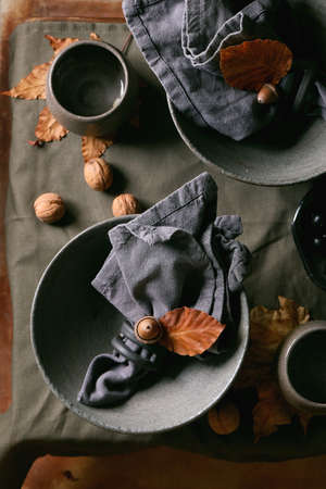 Rustic Autumn Halloween or Thanksgiving table setting with empty craft ceramic tableware, grey rough bowls and cups on linen tableclothの写真素材