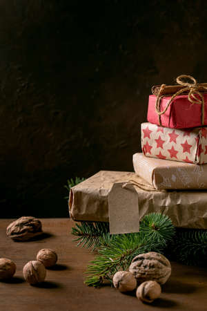 Collection of Christmas gift boxes in eco-friendly craft paper decorated by natural nuts and cinnamon sticks on wooden table with fir tree branches.の写真素材