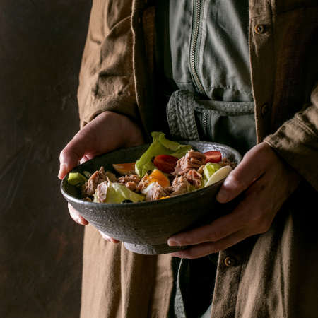 Woman hold in hand bowl of nicoise salad with canned tuna fish, olives and eggs.の写真素材
