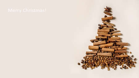 Aromatic spices cinnamon sticks and different coffee beans as Christmas tree shape over beige paper background. Xmas greetings coffee lovers. Banner sizeの写真素材