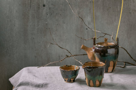 Craft handmade ceramic teapot kettle with cup of hot green tea for tea ceremony standing on linen tablecloth.の写真素材