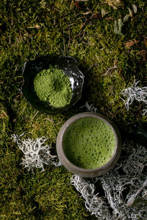 Traditional japanese hot green frothy tea matcha in ceramic cup and powdered matcha over forest moss as background. Healthy natural drink. Flat layの写真素材
