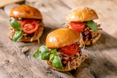 Set of homemade mini burgers with stew beef, tomatoes and basil on wooden background. Modern delicious fast foodの写真素材