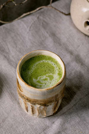 Close up of traditional japanese hot green frothy tea matcha latte in handmade ceramic cup standing on grey linen tablecloth. Healthy drinkの写真素材