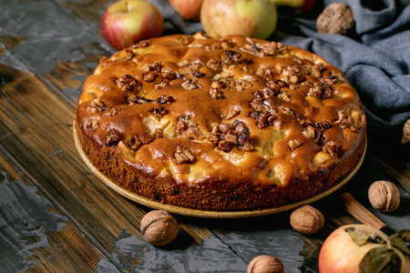 Homemade apple and walnuts cake Charlotte on plate with fresh gardening apples, cinnamons and nuts around on dark wooden plank table. Autumnal home baking.の写真素材