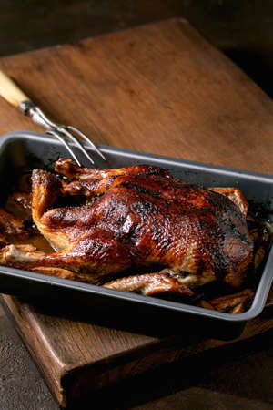 Classic holiday dish roasted honey glazed duck with apples in baking tray with meat fork over wooden table.の写真素材