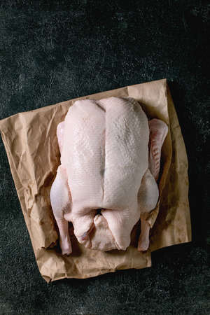 Raw organic uncooked whole duck on crumpled paper over black texture background. Top view, copy spaceの写真素材