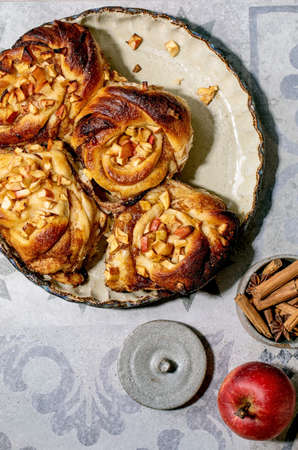 Sweet apple sticky cinnamon rolls buns start to eating in round baking tray standing with gardening...